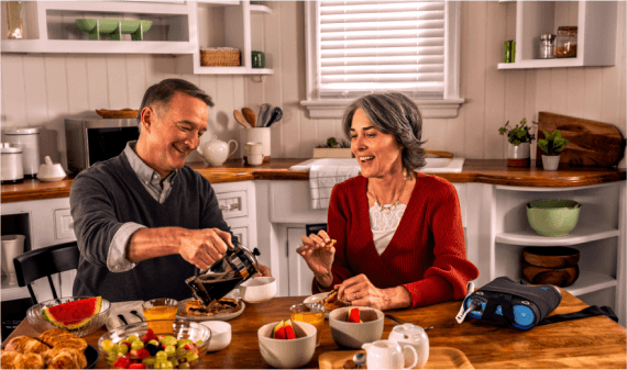 Patient using Optune Lua device while enjoying breakfast with a companion at the kitchen table.