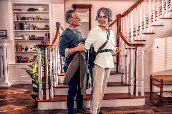 Patient wearing Optune Lua device while preparing to leave home, assisted by a companion.