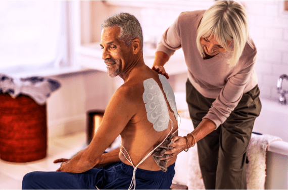 Patient receiving assistance with Optune Lua device while preparing for mNSCLC treatment.